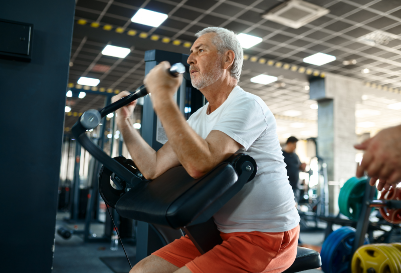Older man performing strength training with weights at the gym to help prevent muscle loss after 50.
