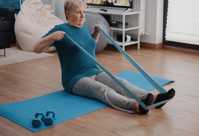 Woman over 60 using resistance band for seated row exercise to maintain muscle and mobility at home.