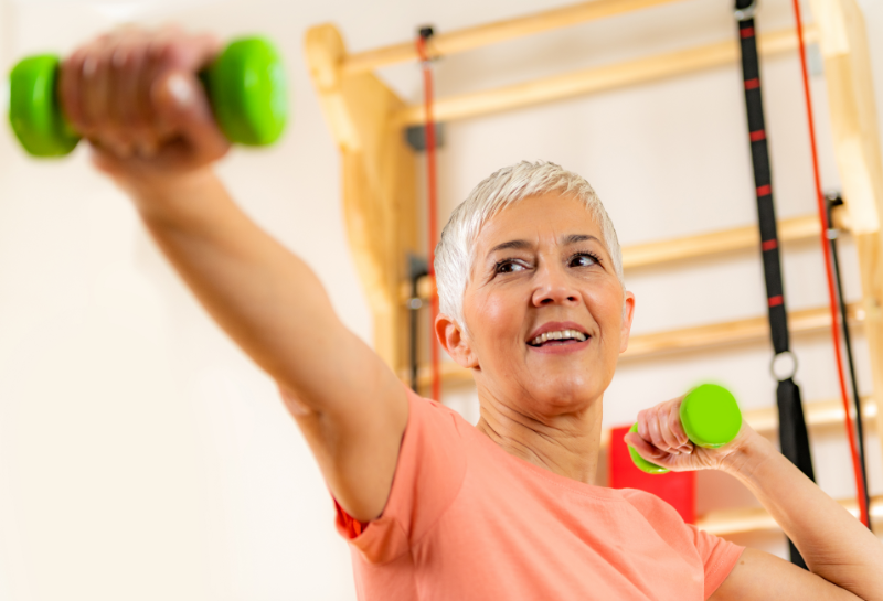 Older woman lifting light dumbbells during home strength training routine to prevent muscle loss after 60.